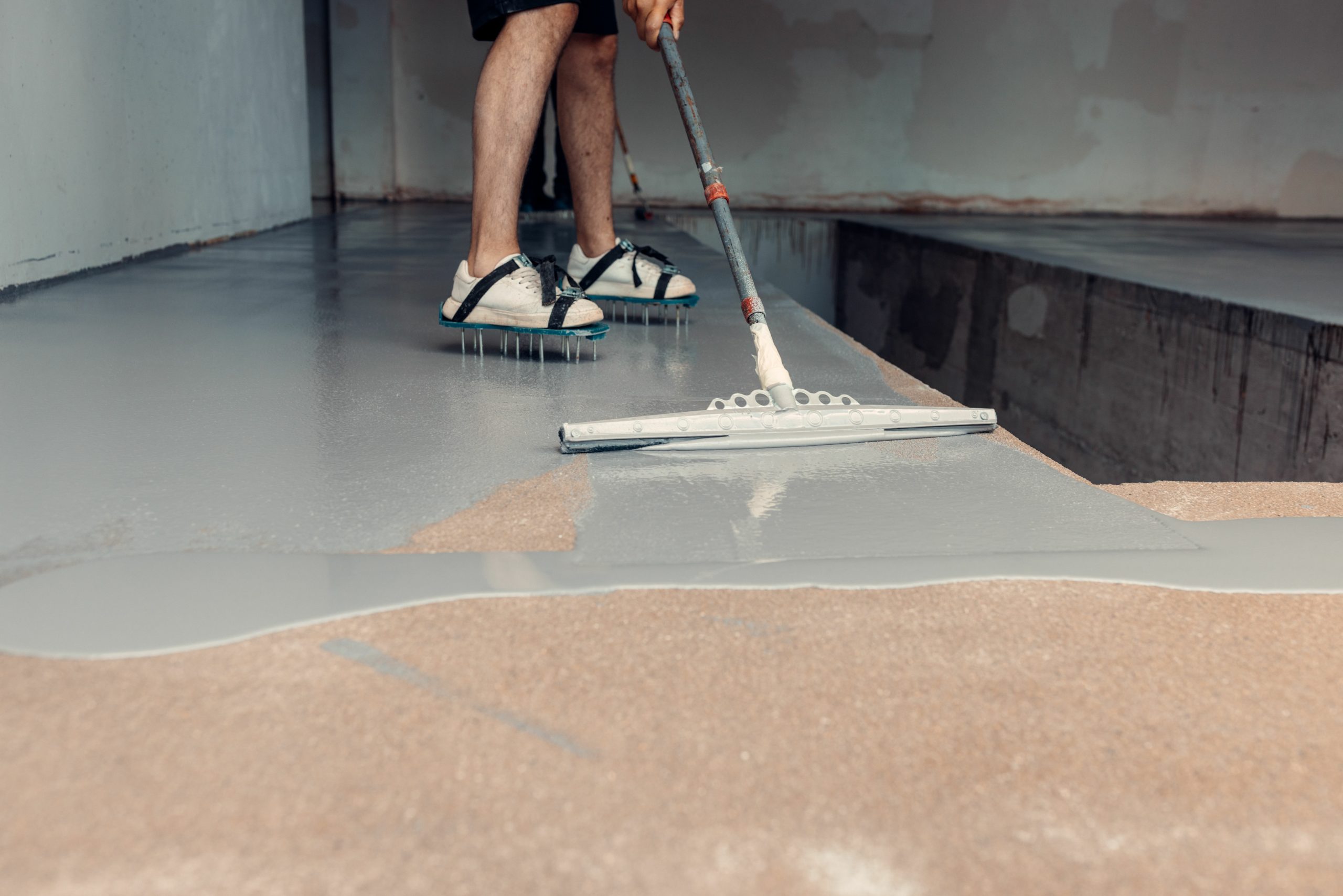 Construction worker applying grey epoxy resin in an industrial hall